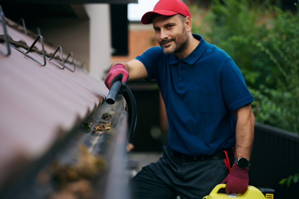 Man cleaning house gutters with a leaf blower during spring maintenance