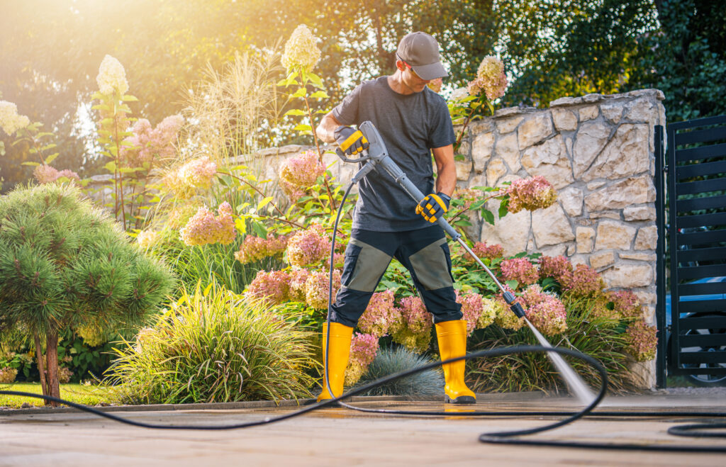 Home service professional pressure washing an outdoor patio and landscaping area